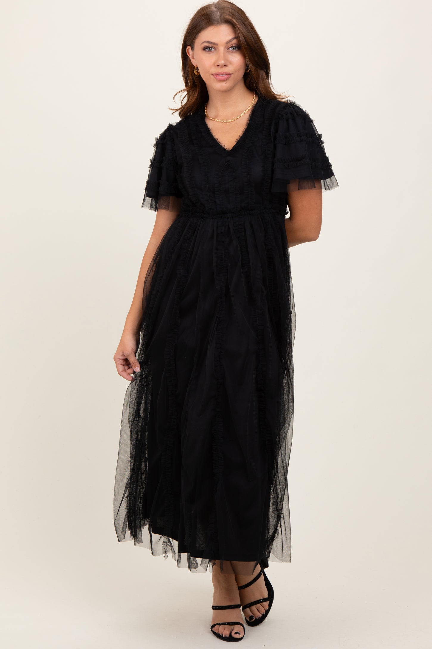 woman wearing a black maxi dress with ruffled sleeves and tulle overlay, standing and posing gracefully