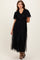 woman wearing a black maxi dress with ruffled sleeves and tulle overlay, standing and posing gracefully