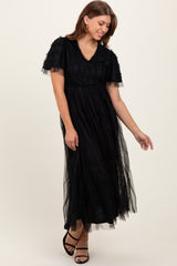 woman wearing a black maxi dress with ruffled short sleeves and a sheer overlay, posing elegantly