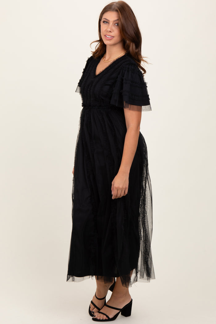 woman wearing a black maxi dress with ruffled sleeves and sheer overlay, standing in a neutral background