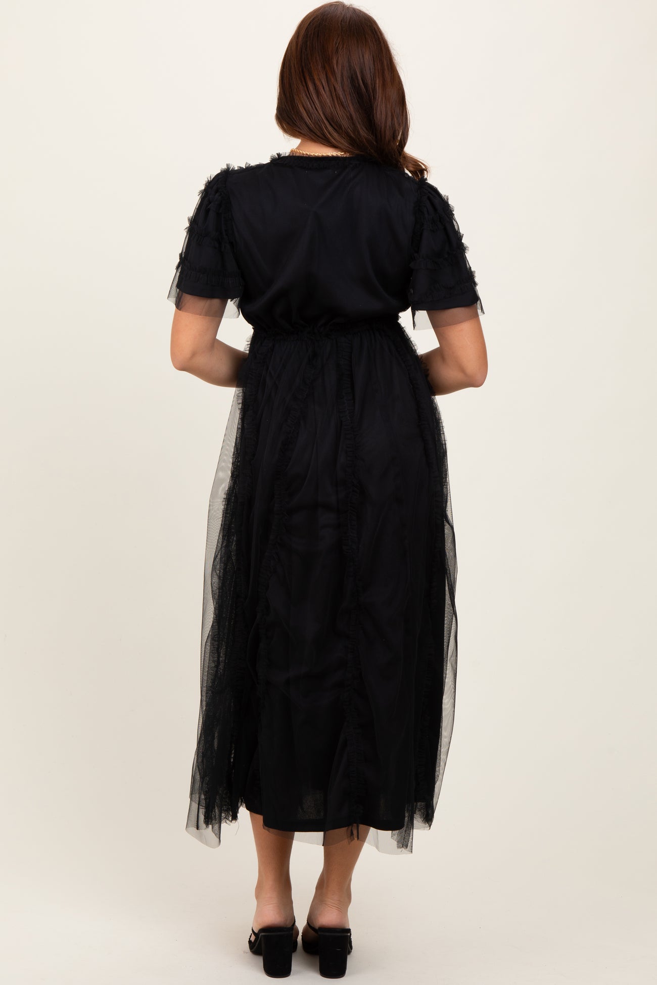 woman wearing a black maxi dress with ruffle details and a sheer overlay, shown from the back