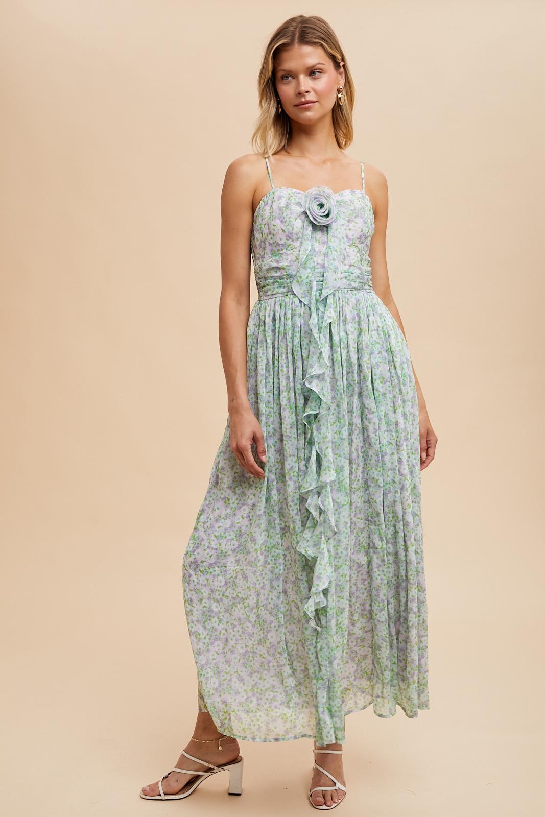 woman wearing a floral maxi dress with a ruffled detail and a rose accent, styled with strappy heels