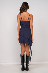 woman wearing a navy blue spaghetti strap mini dress with ruffled layers and a flowing back detail