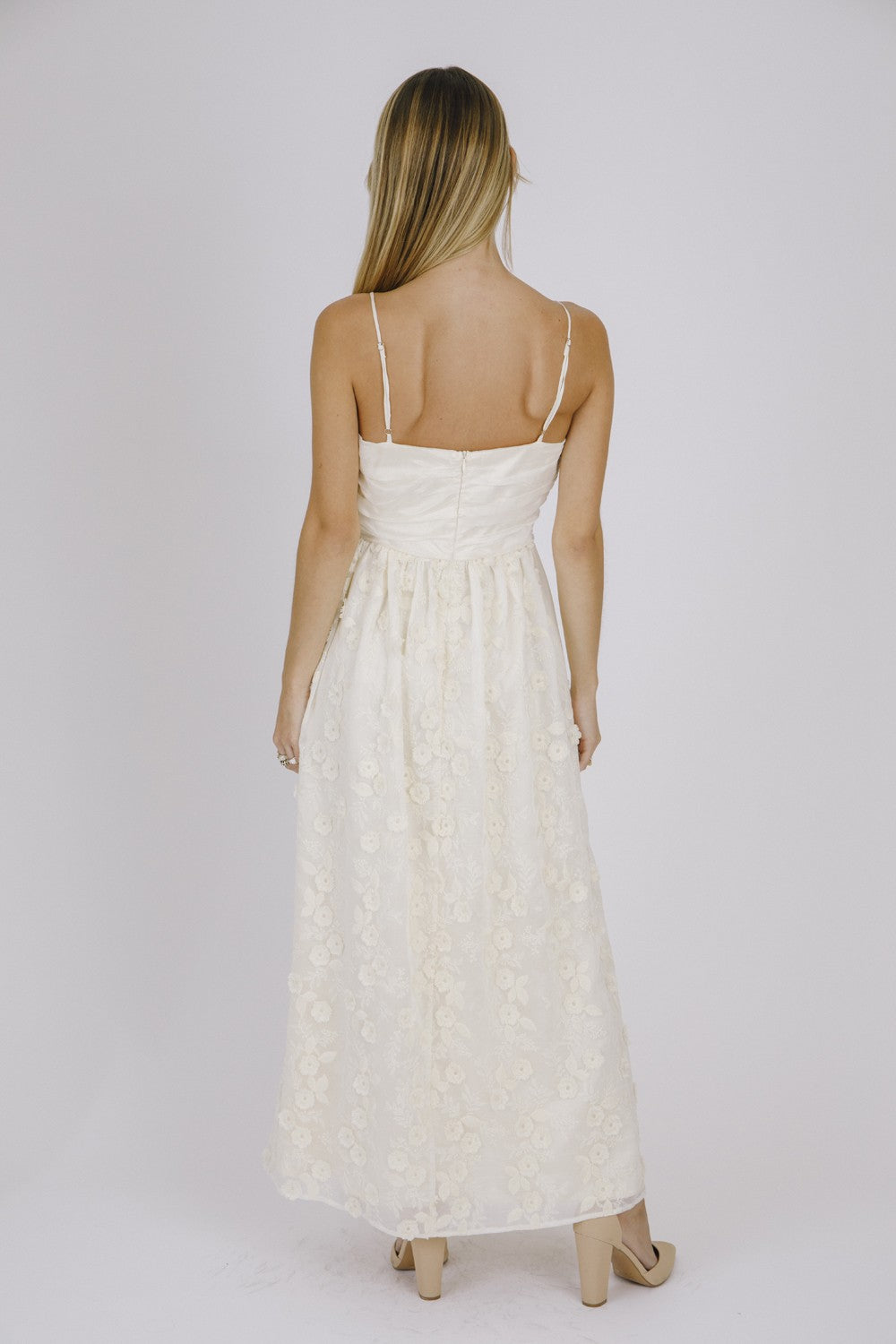 woman wearing a cream maxi dress with floral embroidery and adjustable spaghetti straps, seen from the back