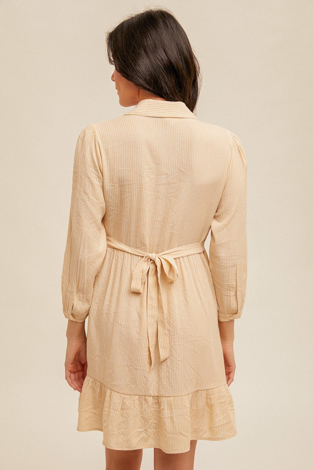 woman wearing a lightweight beige striped shirt dress with a cinched waist and ruffled hem, shown from the back