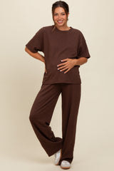 woman wearing a brown maternity waffle knit short sleeve top and matching wide-leg pants, holding her baby bump