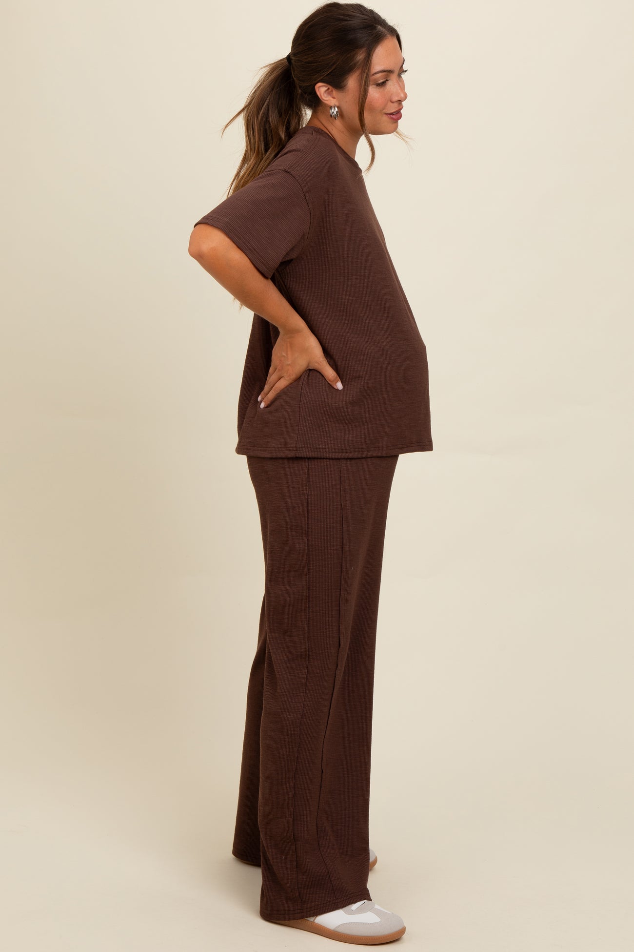 woman wearing a brown maternity top and matching pants, showcasing her baby bump with a relaxed fit and side profile view