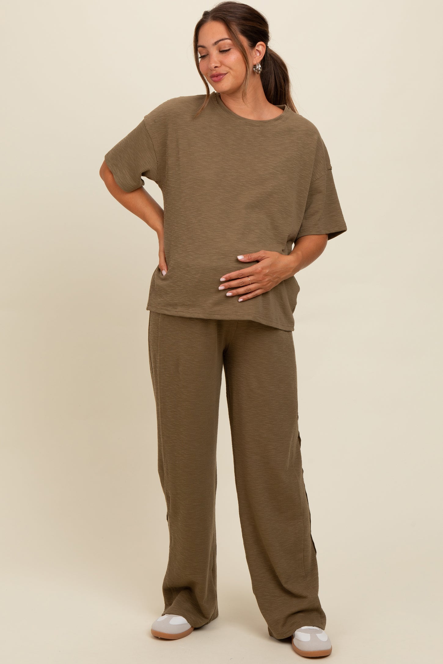 woman wearing a brown ribbed maternity top and matching pants, holding her baby bump