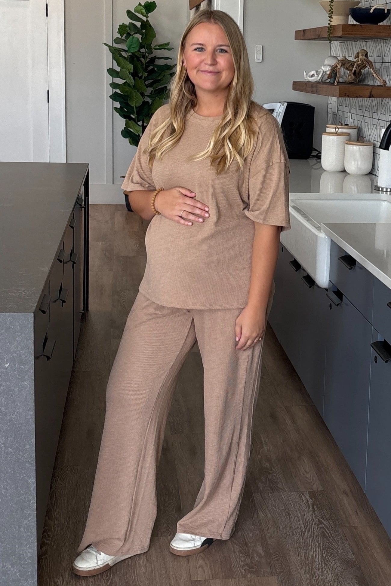 woman wearing a beige maternity lounge set with a relaxed fit and holding her baby bump in a modern kitchen