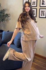 woman wearing a light brown maternity loungewear set with a short sleeve top and wide-leg pants, showing her baby bump
