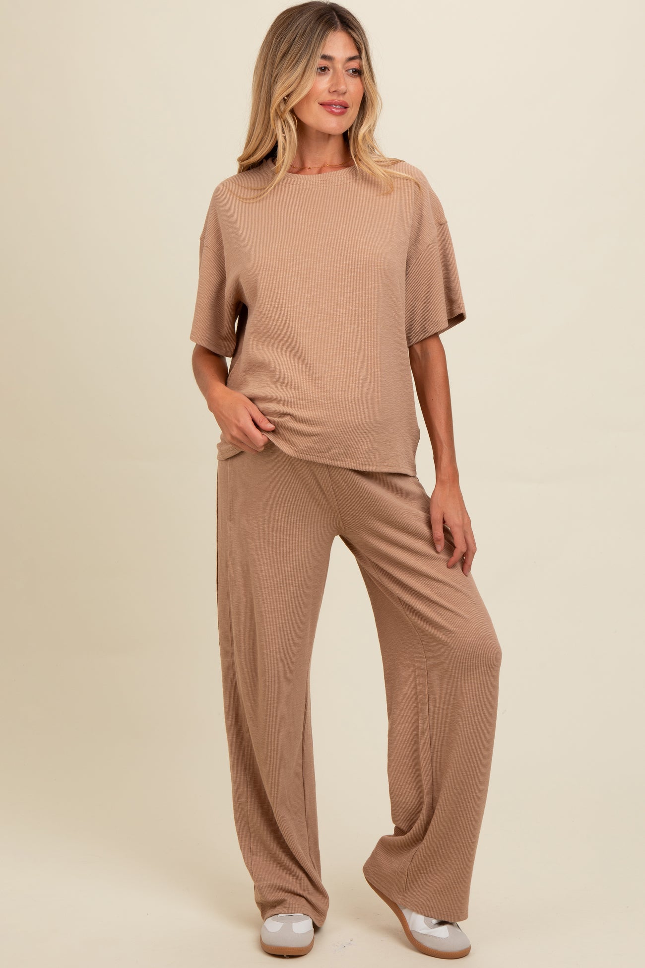 woman wearing a beige maternity loungewear set with a short sleeve top and wide-leg pants