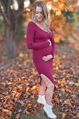 woman wearing a burgundy ribbed maternity dress with a side slit and holding her baby bump in a fall setting