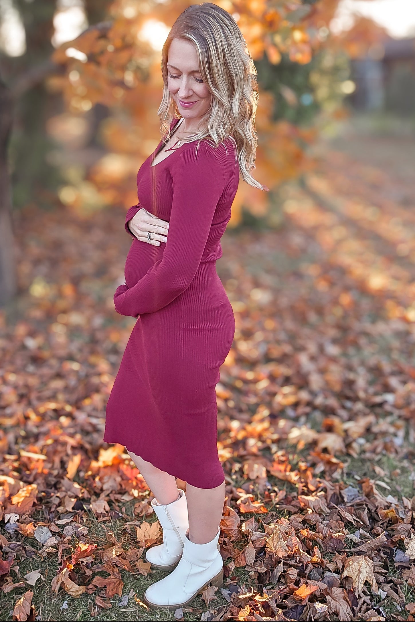 woman wearing a burgundy ribbed maternity dress and showing her baby bump with autumn leaves in the background