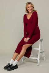 woman wearing a burgundy ribbed maternity dress with a side slit and a visible baby bump, sitting on a white stool