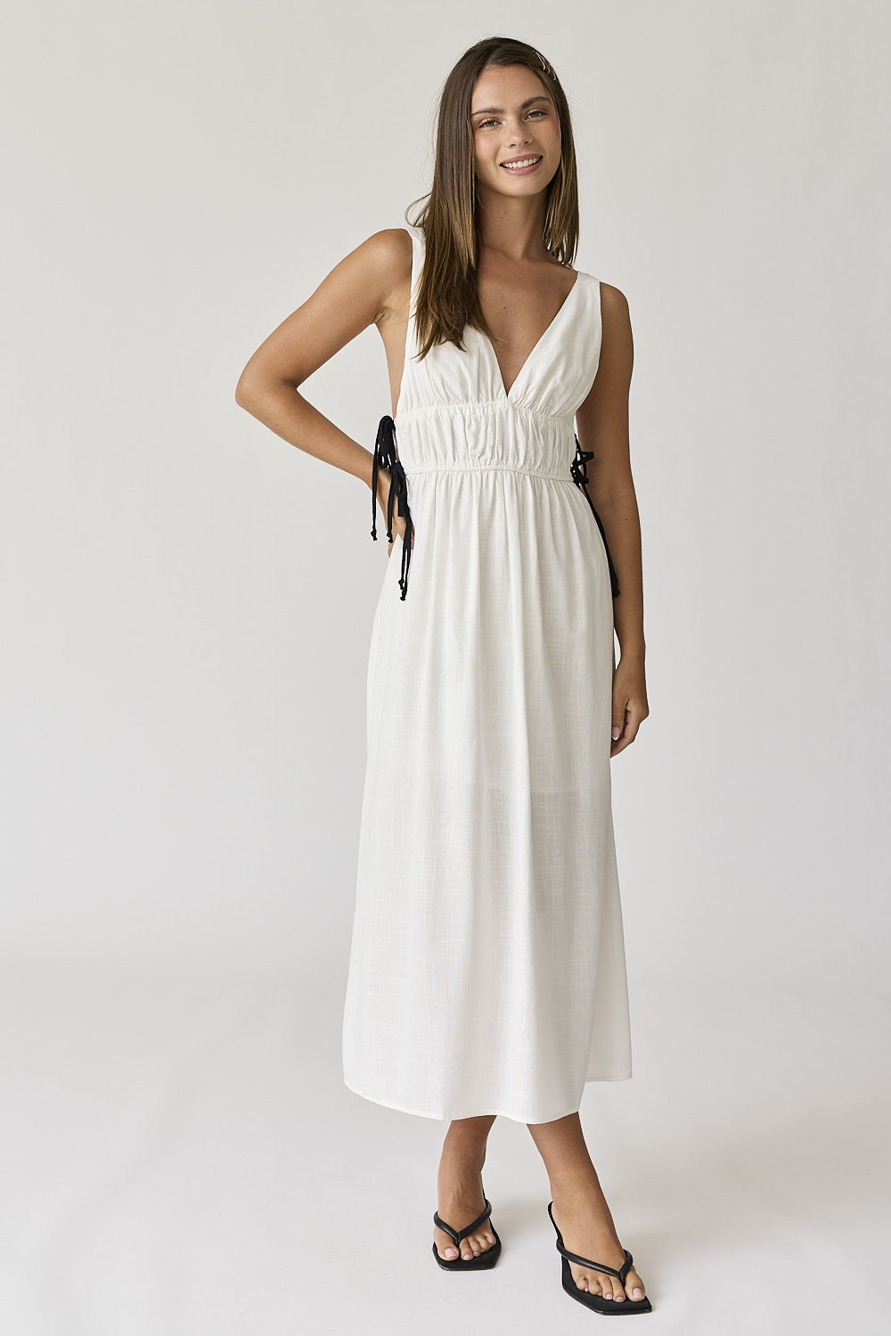 woman wearing a white long maxi dress with adjustable tie straps and a v-neckline, styled with black flip-flops