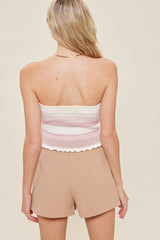 woman wearing a striped pink and white tube top with a scalloped hem and beige high-waisted shorts