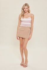 woman wearing a strapless pink and white striped top with a beige mini skirt, standing against a neutral background
