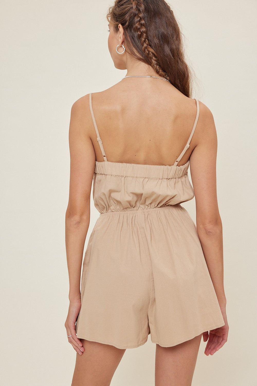 woman wearing a beige sleeveless romper with an elastic waist and open back style