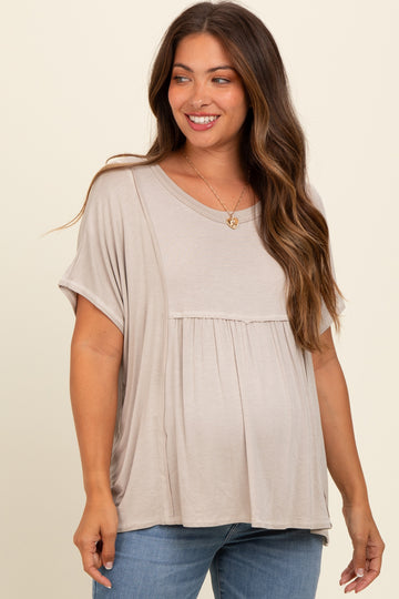 woman wearing a beige maternity top with a gathered waist and short sleeves, showing her baby bump