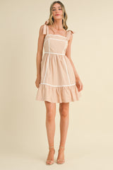 woman wearing a light pink sleeveless dress with tie straps and ruffle hem details