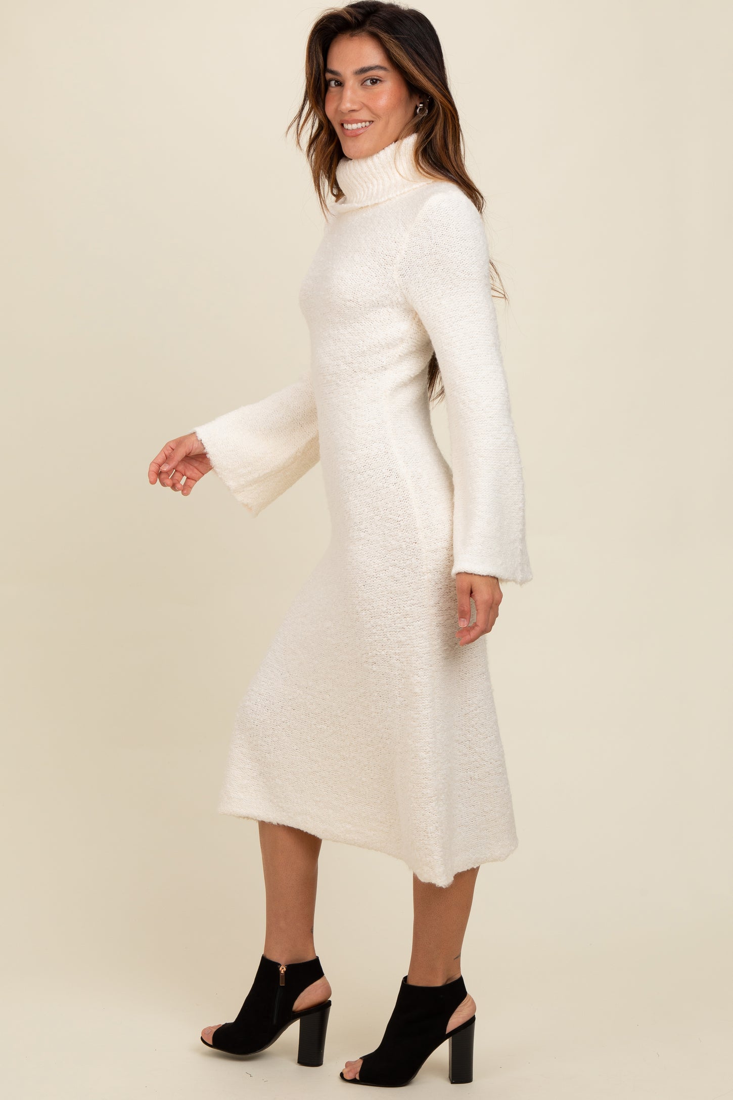 woman wearing a white knit long sleeve turtleneck dress with bell sleeves and a mid-length hem