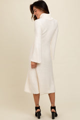 woman wearing a cream long sleeve sweater dress with a cowl neck and flared sleeves, shown from the back