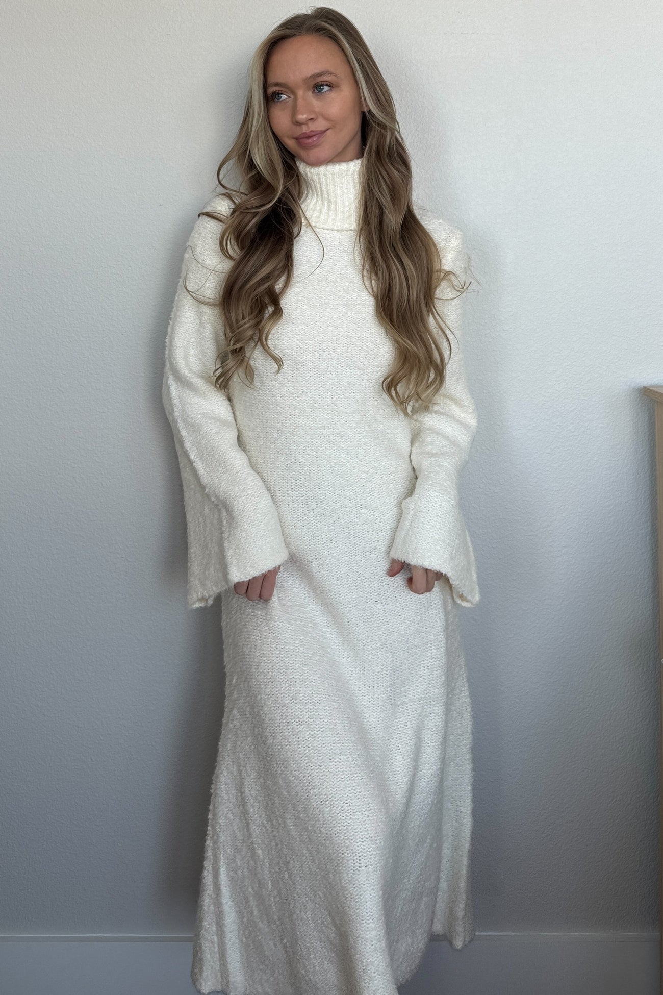 woman wearing a white long sleeve turtleneck dress with bell sleeves and a maxi length