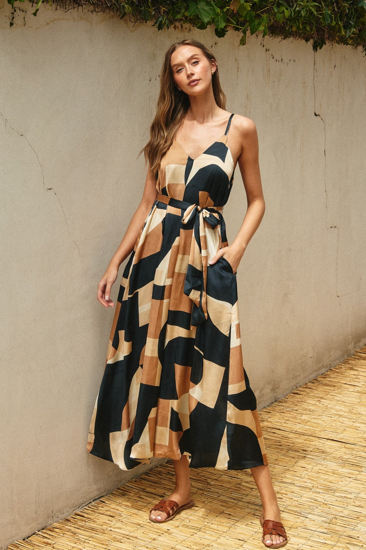 woman wearing a patterned maxi dress with spaghetti straps and pockets, featuring a tie waist detail