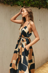 woman wearing a sleeveless maxi dress with a geometric print in brown and navy, featuring a tie waist and pockets