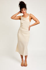 woman wearing a cream sleeveless midi dress with a draped neckline and a relaxed fit