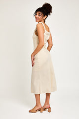 woman wearing a beige sleeveless midi dress with a relaxed fit and ruffled straps, standing against a light background