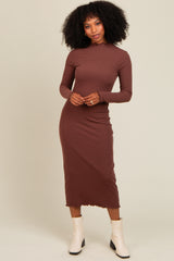 woman wearing a brown ribbed long sleeve midi dress with a scalloped hem and standing in front of a neutral background