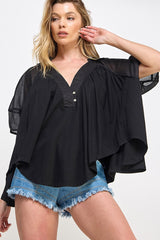 woman wearing a black flowy top with a v-neck and short sleeves paired with denim shorts