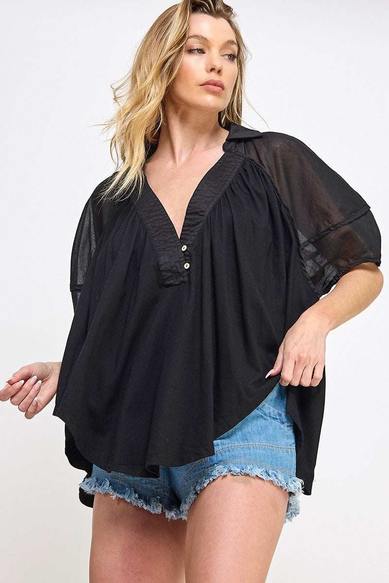 woman wearing a black loose fit blouse with a v-neck and short sheer sleeves, paired with denim shorts