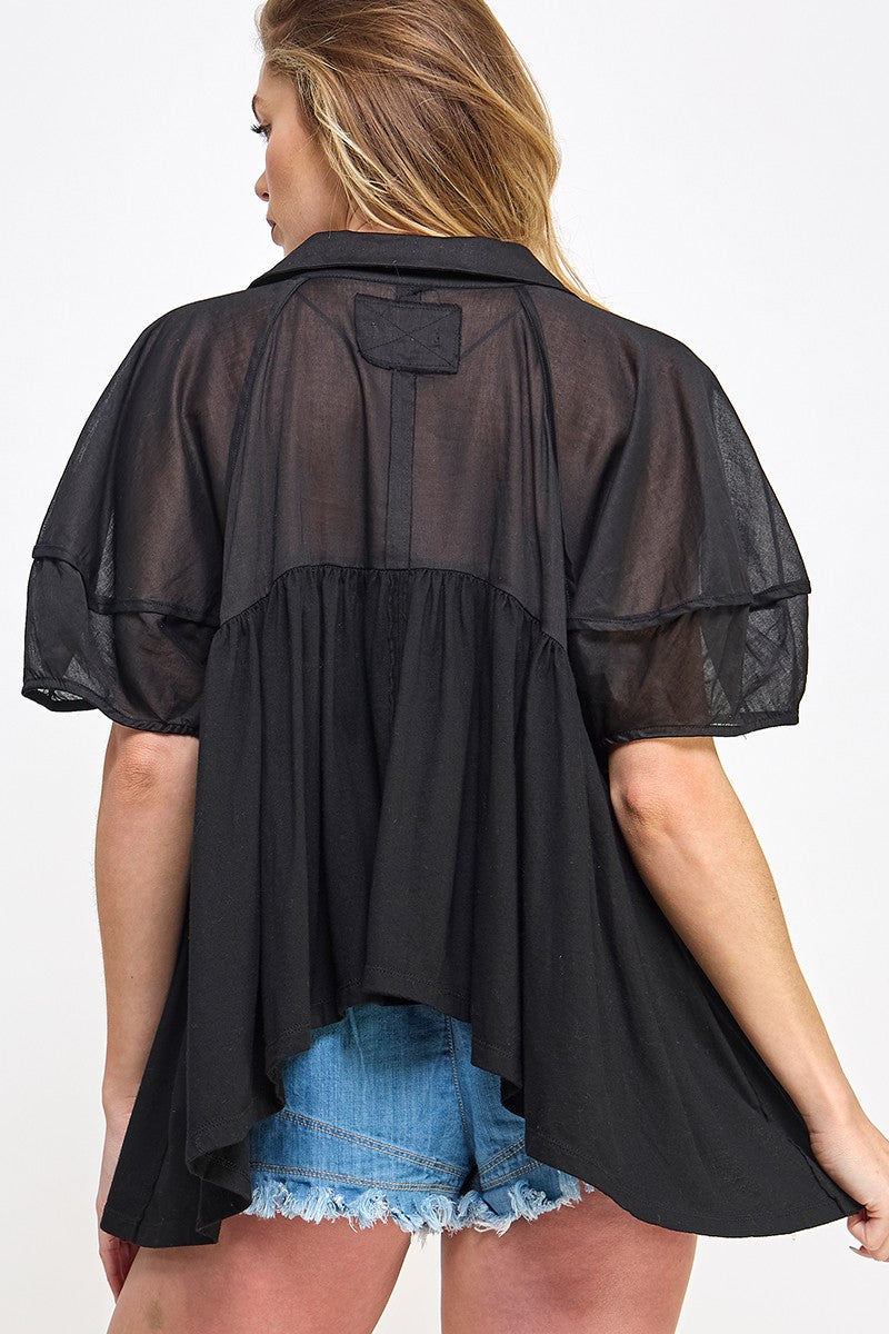 woman wearing a black sheer top with short sleeves and a flowy back, paired with denim shorts
