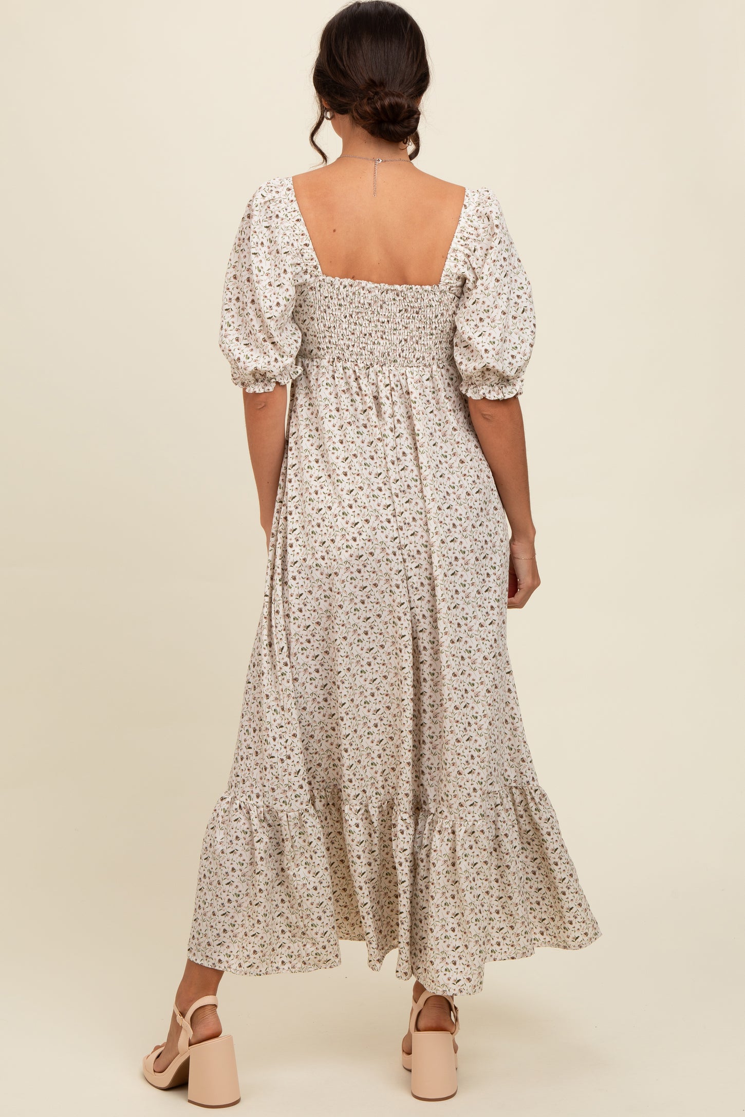 woman wearing a backless white floral maxi dress with puff sleeves and a ruffled hemline