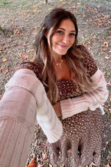 woman wearing a brown floral maternity dress with a cream knitted cardigan, holding her baby bump outdoors