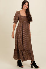woman wearing a brown floral maxi dress with puff sleeves and a tiered hem, paired with black open-toe heeled sandals