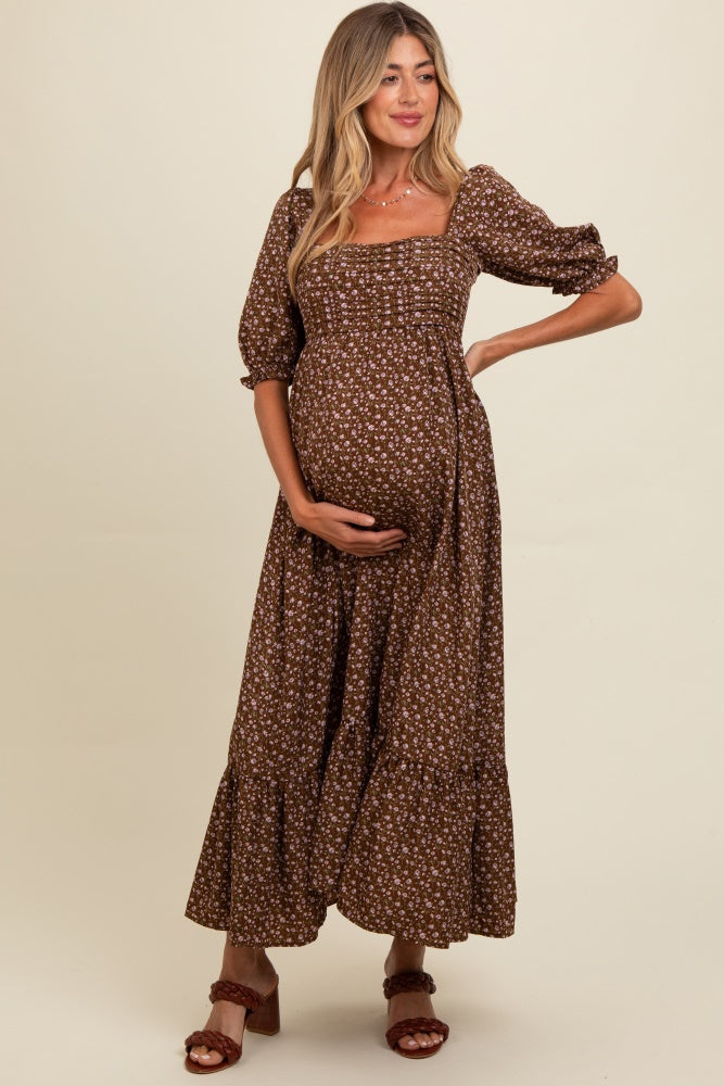 woman wearing a brown floral maternity dress, standing with her hand on her baby bump