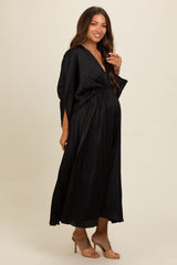 woman wearing a black pleated maternity dress with a deep V-neckline and a fitted waist, showcasing her baby bump