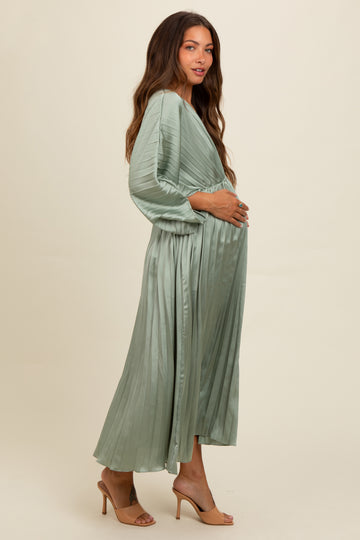 woman wearing a sage green pleated maternity dress with long sleeves and a visible baby bump