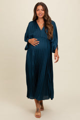 woman wearing a dark teal pleated maternity dress and gently cradling her baby bump