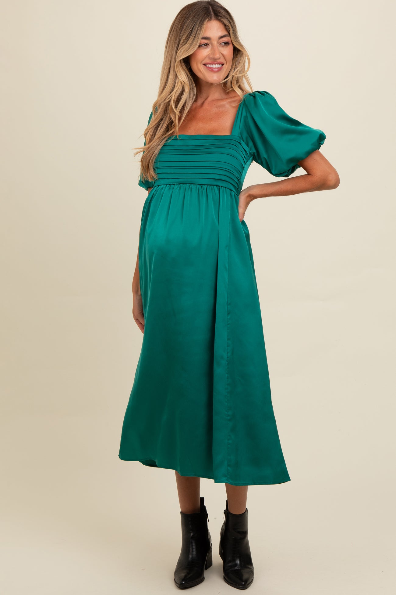 woman wearing a green satin maternity dress with puff sleeves and a gathered bodice, showing off her baby bump