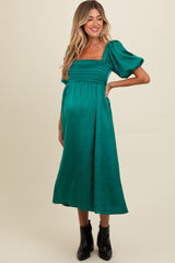 woman wearing a green satin maternity dress with puff sleeves and a gathered bodice, showing off her baby bump