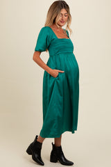 woman wearing a green midi maternity dress with puff sleeves and pockets, showcasing her baby bump