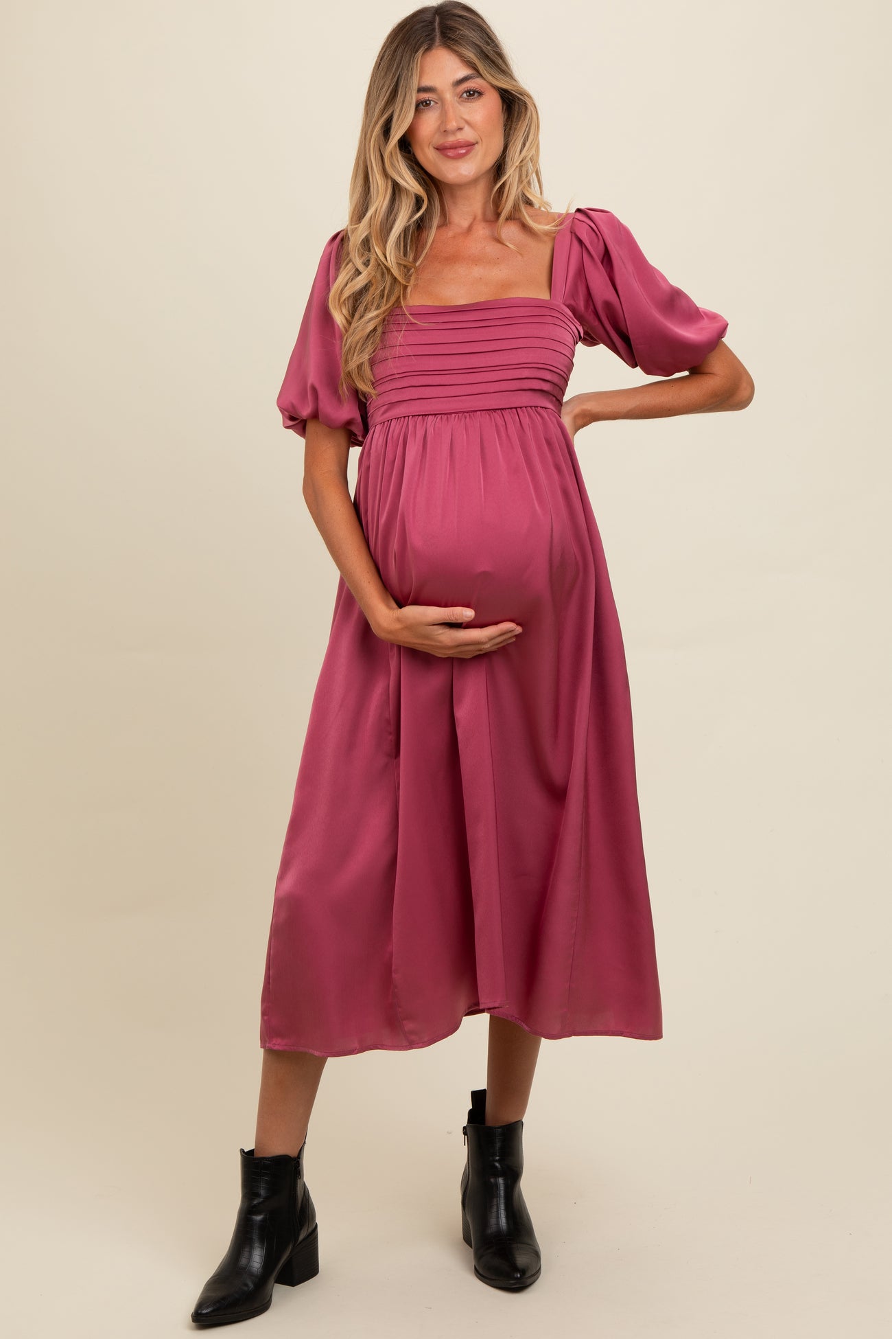woman wearing a pink maternity dress with puff sleeves and a square neckline, holding her baby bump