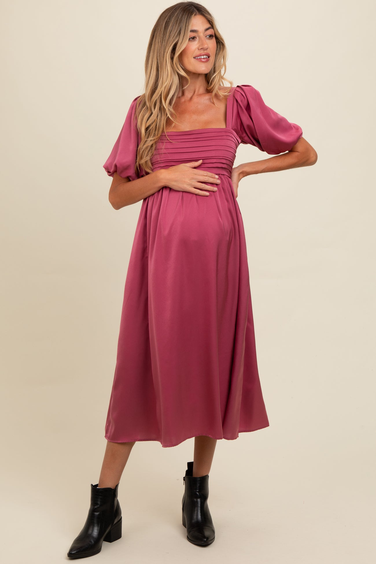 woman wearing a dark pink maternity dress with puff sleeves and a gathered bodice, gently holding her baby bump