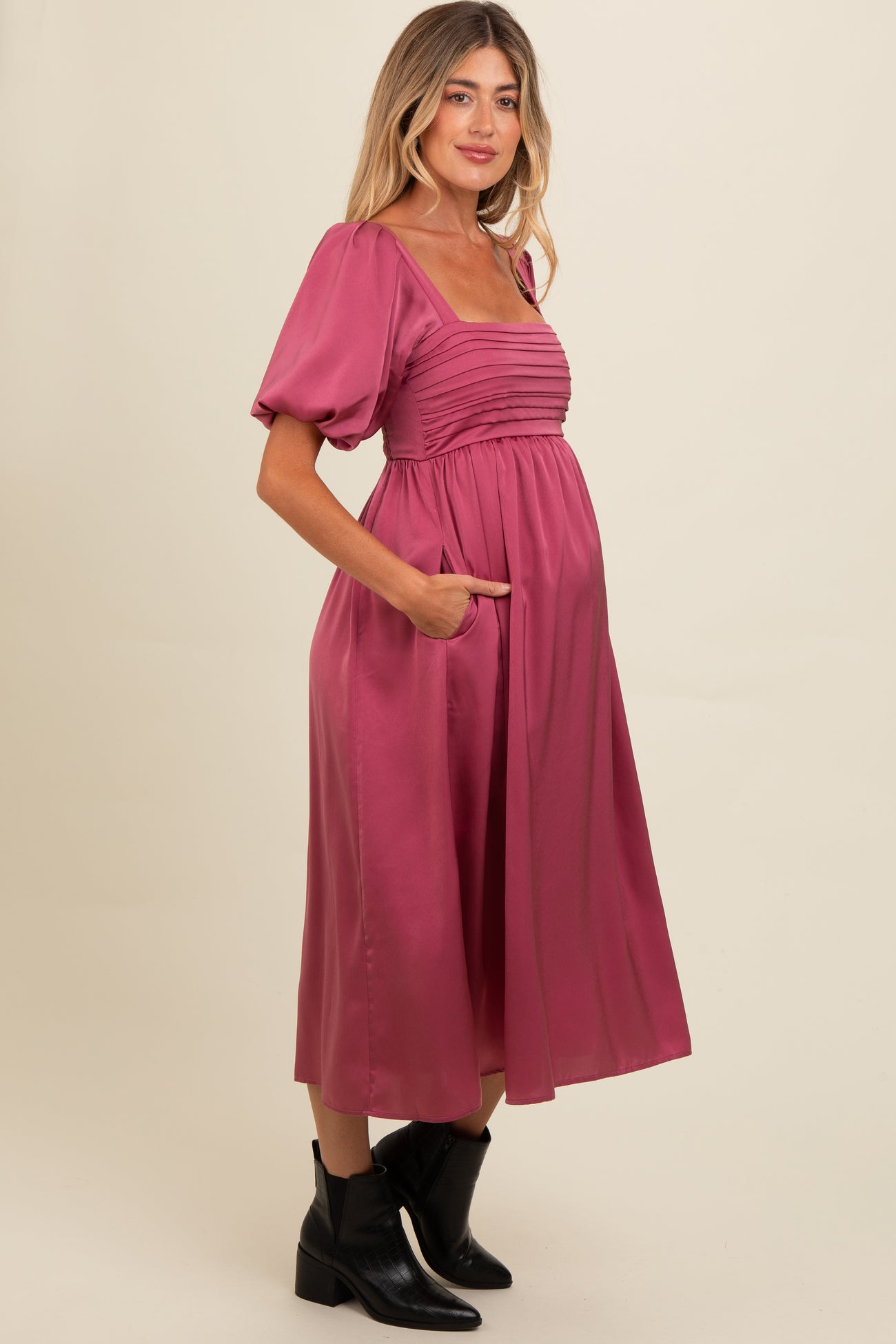 woman wearing a pink midi maternity dress with puff sleeves and side pockets, showcasing her baby bump
