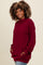 woman wearing a burgundy oversized cowl neck sweatshirt with pockets and long sleeves, styled with light blue jeans