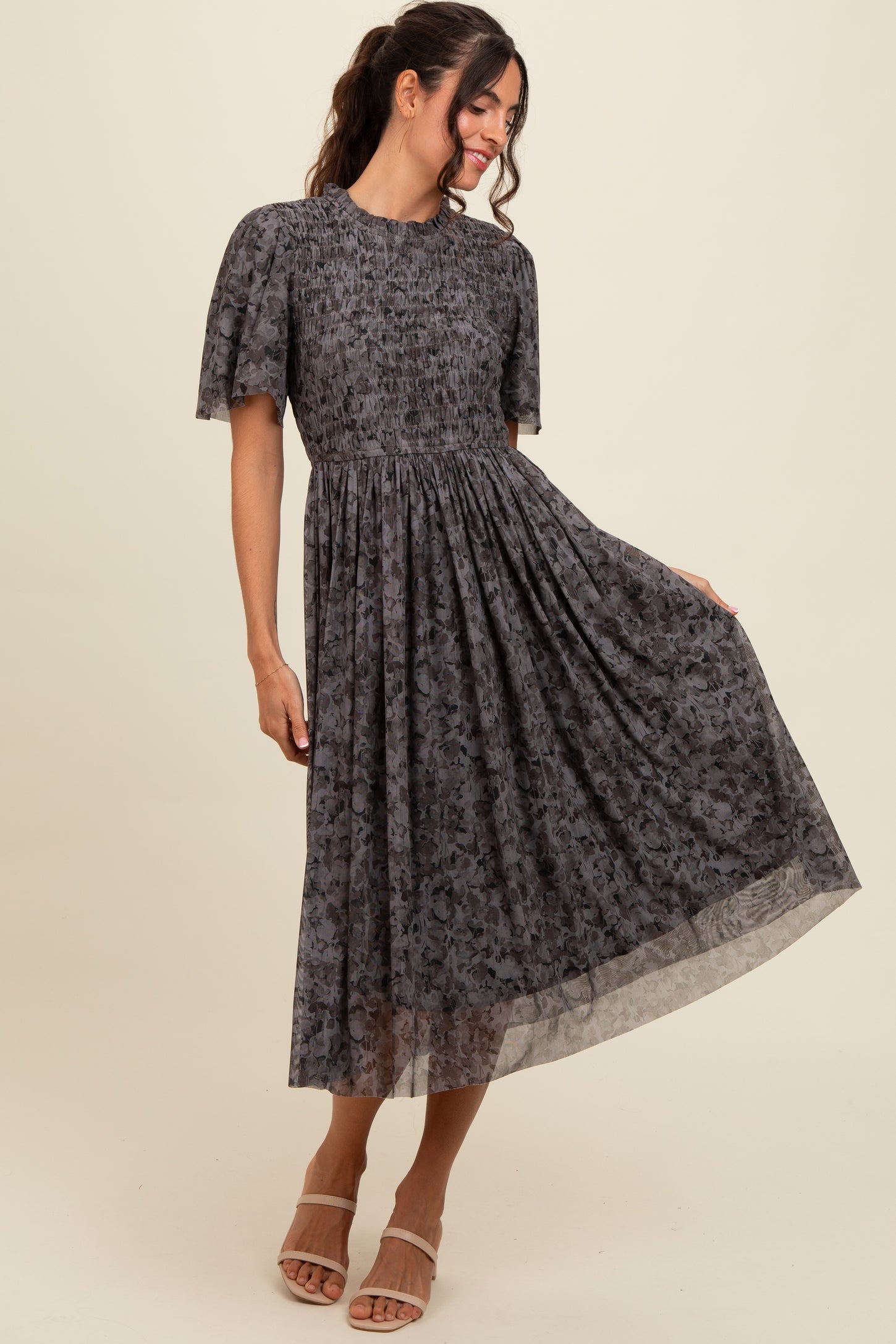 woman wearing a dark floral midi dress with puff sleeves and a cinched waist, posing with one hand on her hip